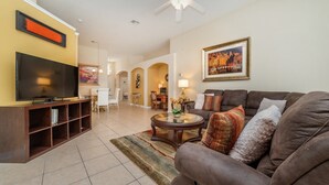 A living room with a television, sofa, and coffee table. There is a dining area with chairs and a table in the background. - Luxury Villa with Private Pool on Windsor Palms Resort, Orlando Villa 4885 (Orlando)