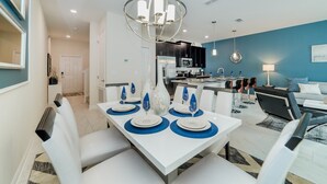 A modern dining area with a white table set for four, a kitchen in the background, and a blue accent wall. - Beautiful Townhome with first class amenities on Storey Lake Resort, Orlando Townhome 4897 (Orlando)