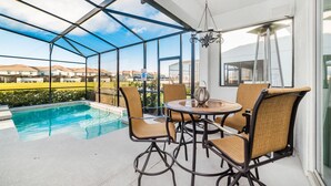 Un espacio exterior cubierto con piscina, sillas de mimbre y una mesa.