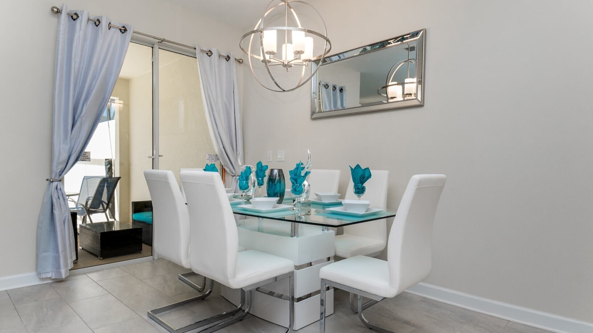 Uma área de refeições com mesa de vidro, cadeiras brancas e vasos azuis decorativos.