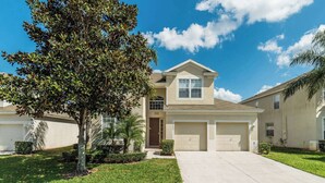 A two-story house with a garage, a front yard with a tree, and a clear blue sky.