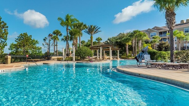 Una piscina azul cristalina con sillas de descanso y palmeras alrededor.