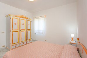 A bedroom with a bed, a wardrobe, a nightstand, and a window with curtains.