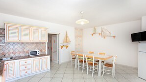 Een keuken met een magnetron, een eettafel met stoelen, een plafondventilator en een televisie.