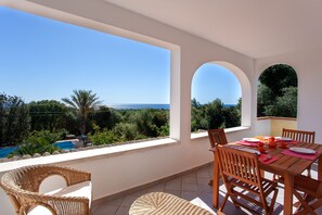 A terrace with a dining table, chairs, and a view of the sea.
