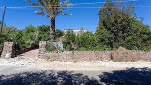 A stone wall, a palm tree, and a building in the background. - Holiday Apartment 'Pavoncella' with Wi-Fi, Garden & Shared Pool (Orosei)