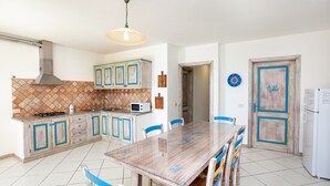 A kitchen with a tiled backsplash, a stove, a microwave, and a dining table with chairs. - Holiday Apartment 'Pavoncella' with Wi-Fi, Garden & Shared Pool (Orosei)