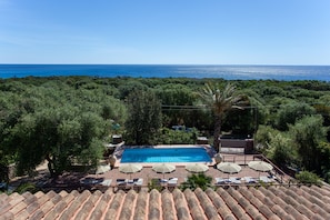 A rooftop pool with a view of the sea, surrounded by trees and umbrellas.