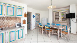 A kitchen with a dining area, a microwave, cabinets, and a television. - Holiday Apartment 'Pavoncella' with Wi-Fi, Garden & Shared Pool (Orosei)