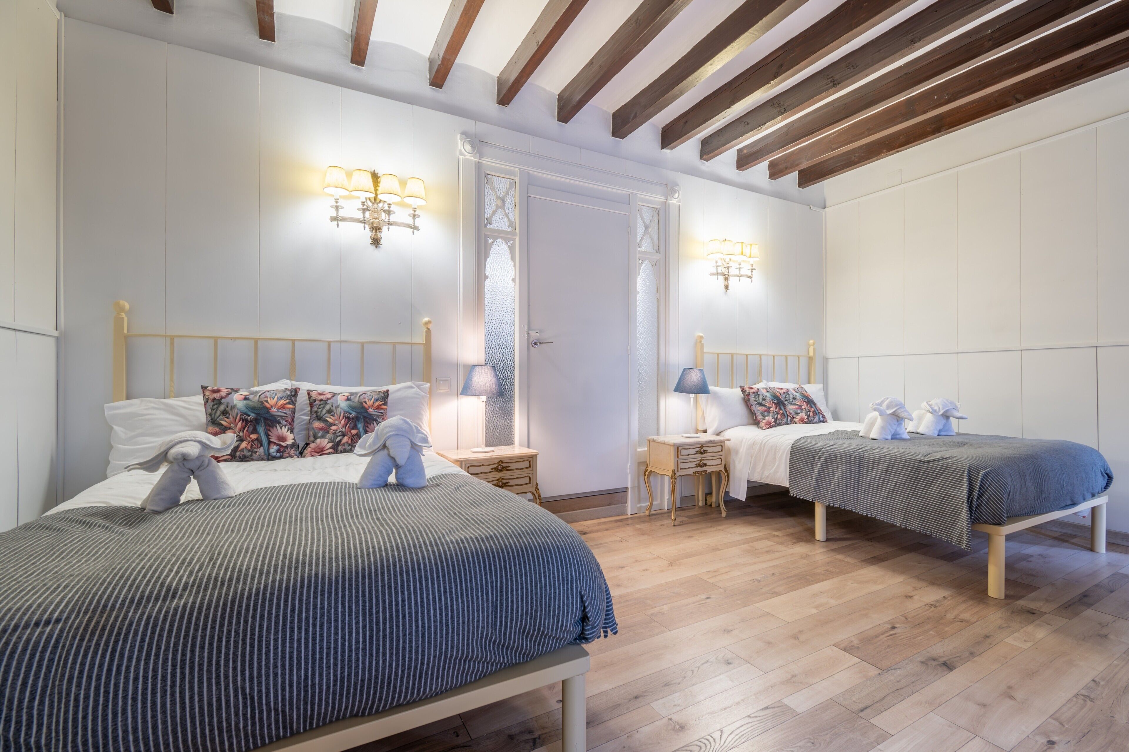 Une chambre avec deux lits, des têtes de lit en bois, des tables de chevet, des lampes et une porte avec des panneaux en verre dépoli.