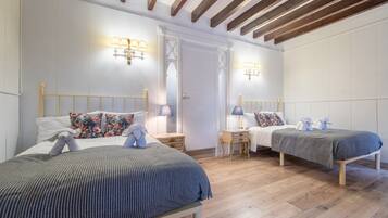Une chambre avec deux lits, des têtes de lit en bois, des tables de chevet, des lampes et une porte avec des panneaux en verre dépoli.