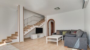 A modern living room with a staircase, a flat-screen TV, a grey sofa, and a white coffee table. - Holiday Home ‘Casa Oasis’ with Pool, Wi-Fi, Air Conditioning & Terrace (Tías)