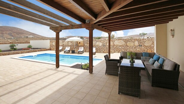 A covered outdoor area with a pool, lounge chairs, a sofa, and a table.