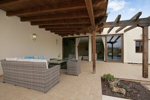 Un patio exterior con mobiliario de mimbre, una pérgola y un pequeño jardín.