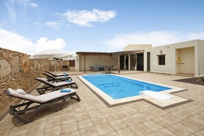 Una piscina con sillones de descanso, un muro de piedra y un patio cubierto.