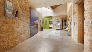 A stone-walled hallway with a tiled floor, a reception desk, and a green room in the background.