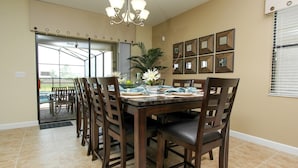 A dining area with a rectangular table, multiple chairs, a chandelier, and framed pictures on the wall.