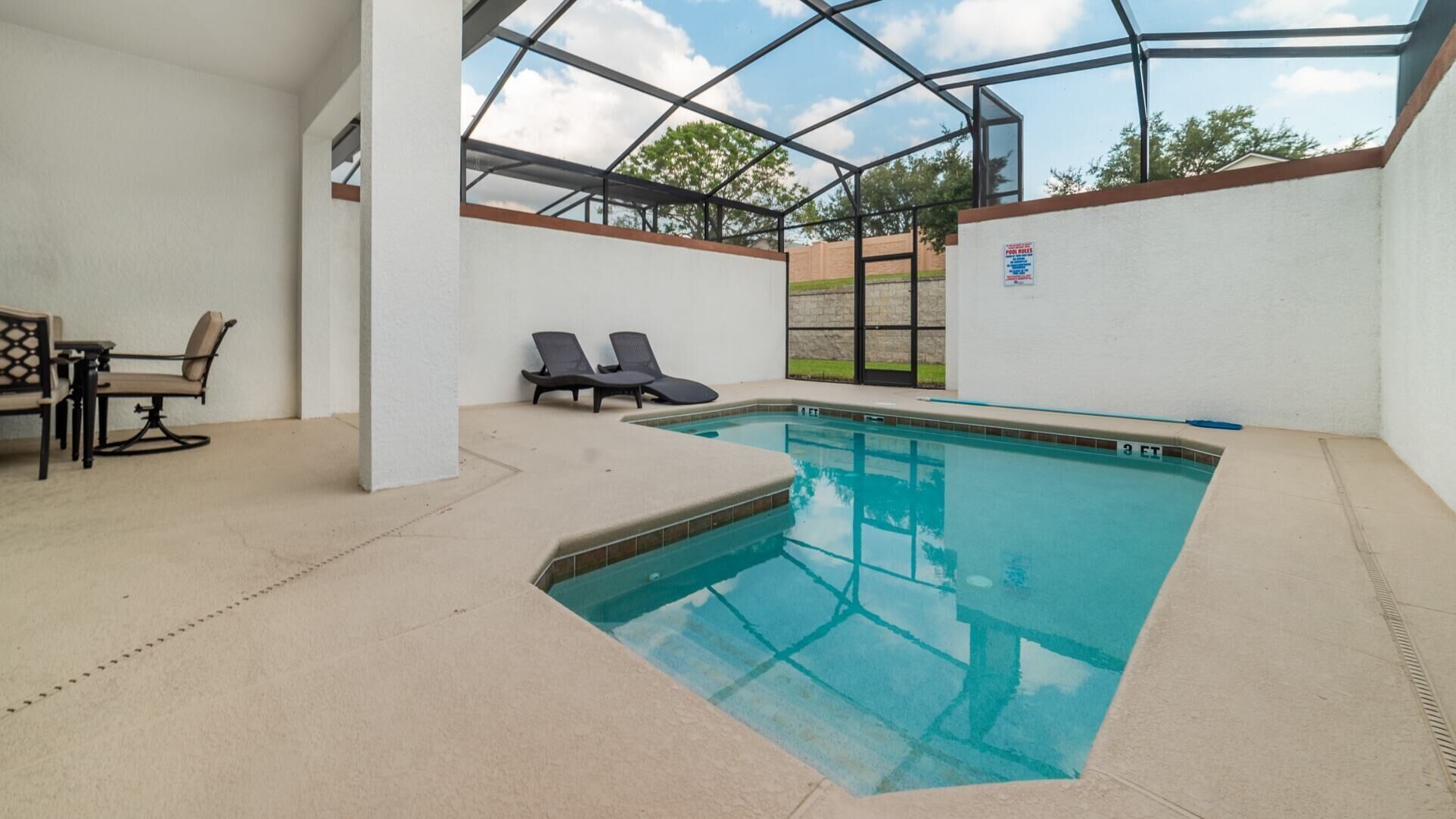 An indoor swimming pool with a glass ceiling, lounge chairs, and a table with chairs.