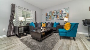 A modern living room with a sofa, coffee table, and armchairs. There are abstract paintings on the wall and a window with curtains. - Luxury Townhome with Private Pool on Champions Gate Resort, Orlando Townhome 4933 (Orlando)