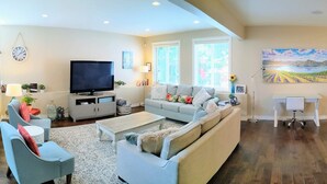 A modern living room with a flat-screen TV, a sofa, a coffee table, and a desk with a chair. - Spacious Westside  Wine Trail Retreat ★★★★★ (West Kelowna)