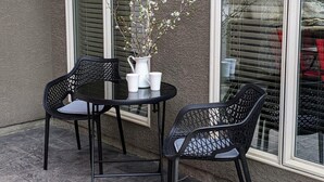 An outdoor patio with a round table and two chairs, a white vase with flowers, and large windows with blinds. - Spacious Westside  Wine Trail Retreat ★★★★★ (West Kelowna)