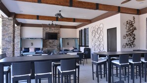 A spacious outdoor dining area with a long table and multiple chairs, a stone fireplace, and a modern wall art piece.