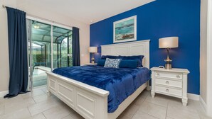 A bedroom with a large bed, two bedside tables, a nightstand, a glass door leading to a balcony, and a painting on the wall.