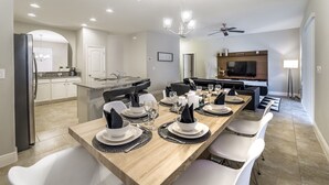 A modern dining area with a long wooden table set for six, white chairs, and a kitchen in the background. - Luxury Villa with Private Pool on Solterra Resort, Orlando Villa 4946 (Orlando)