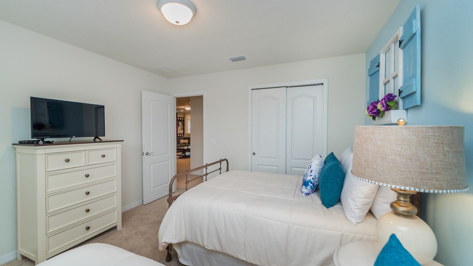 A bedroom with a bed, a dresser, a television, and a lamp.