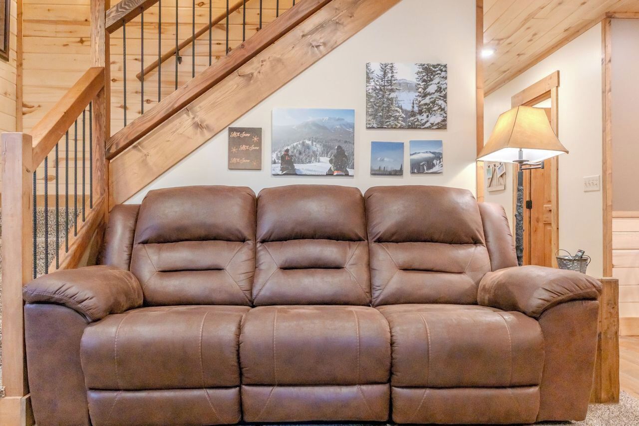 A brown leather sofa in a room with wooden walls and a wooden staircase.