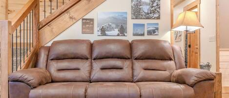 A brown leather sofa in a room with wooden walls and a wooden staircase.