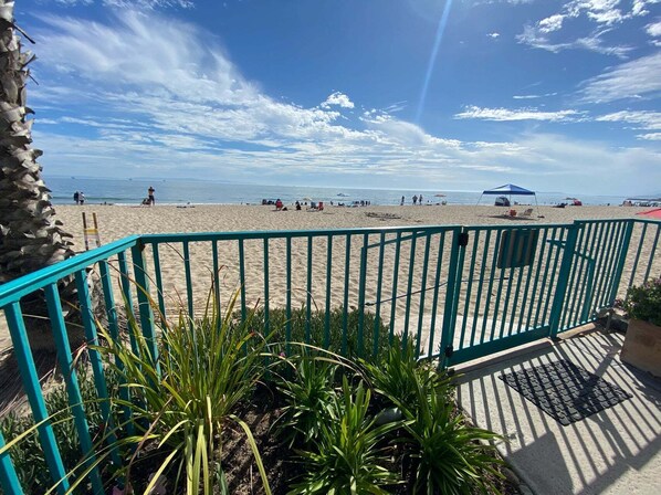 Une vue sur la plage avec une balustrade turquoise, des palmiers et un ciel dégagé.