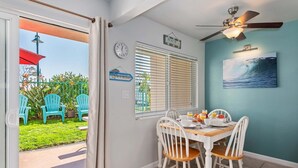 Un coin repas avec une table mise pour le petit-déjeuner, un ventilateur de plafond, une horloge et un panneau décoratif sur le thème de la plage.