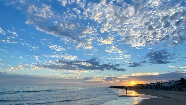 Une plage avec des vagues, un coucher de soleil et un ciel nuageux.