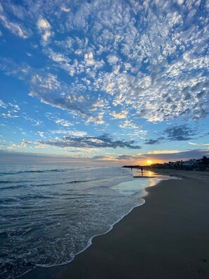 Une plage avec des vagues, un coucher de soleil et un ciel nuageux.