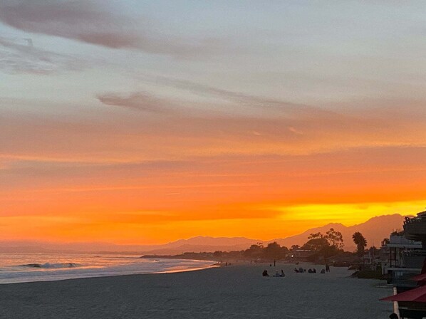 A beach with a sunset, waves, and distant mountains. - Beach Access in 14 Steps | Remodeled Condo with Private Patio (Carpinteria)