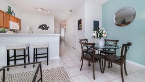 A modern kitchen with wooden cabinets, a white countertop, and a microwave. There is a dining area with a glass table and wooden chairs. - 5 Star Townhome on Windsor Hills Resort with Large Private Pool, Orlando Townhome 4981 (Orlando)