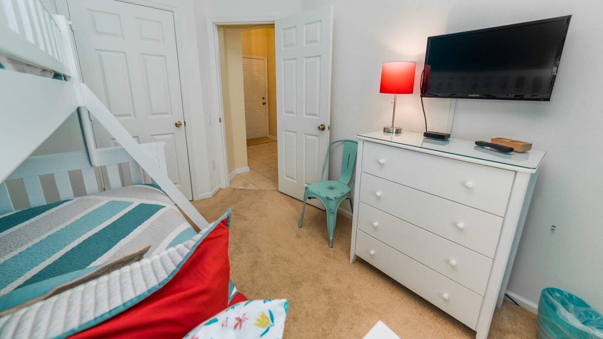 Une chambre avec un lit superposé, une commode, un téléviseur et une chaise.