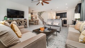 A modern living room with a flat-screen TV, a ceiling fan, and a dining area with a staircase.