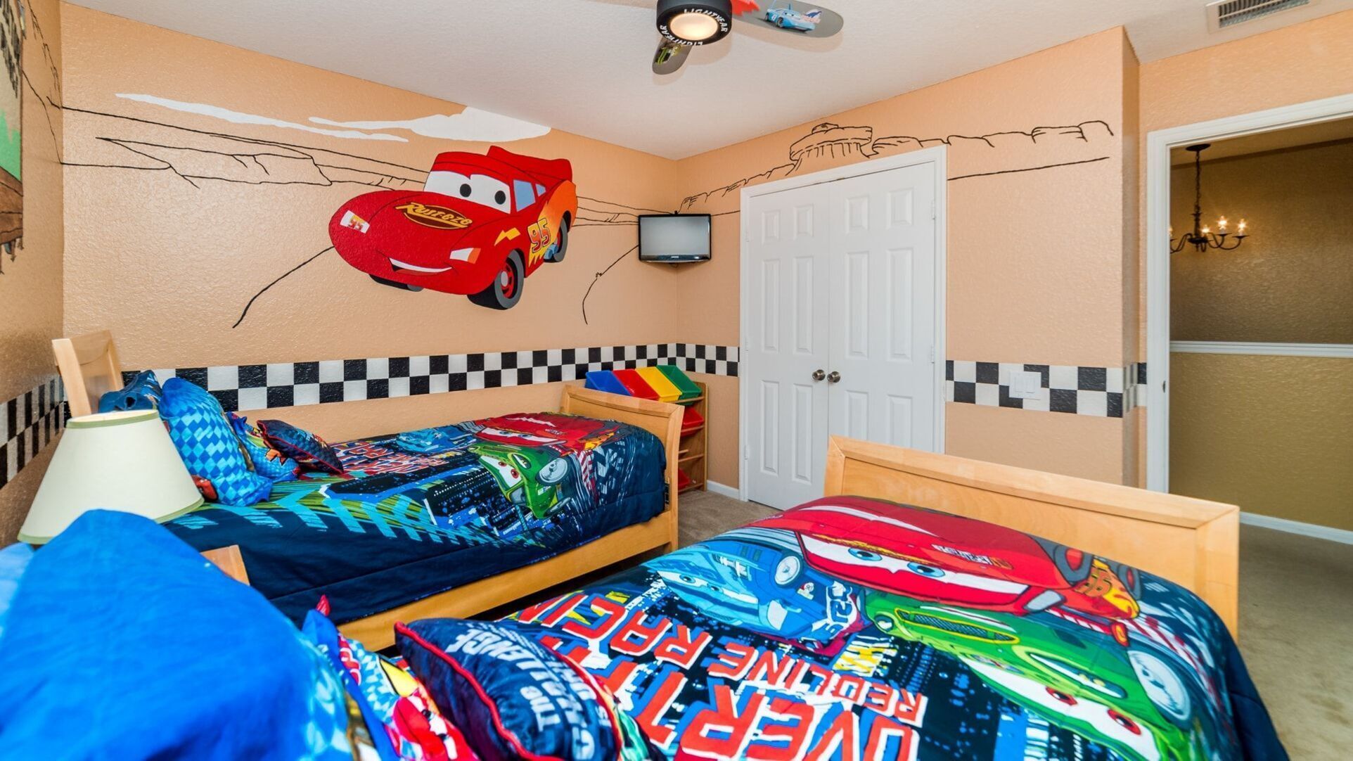 A child's bedroom with a race car theme, including a bed with a car bedspread, a wall mural, and a ceiling fan.