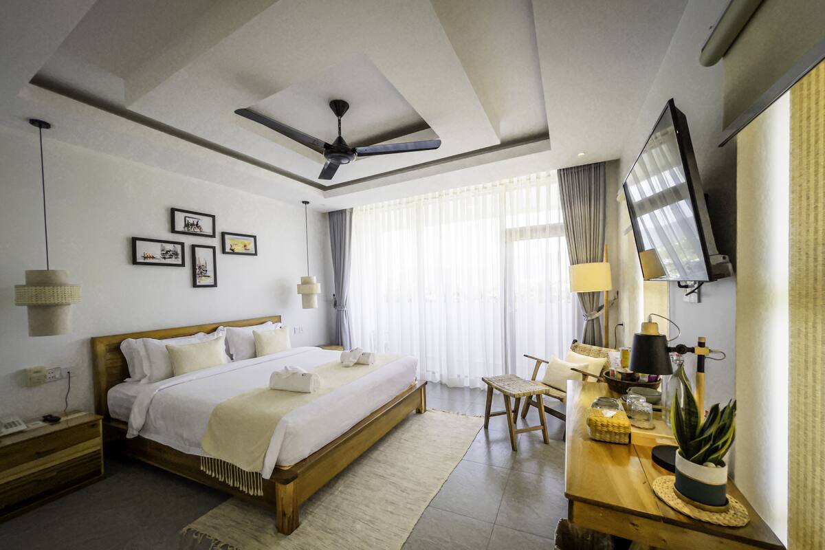 A hotel room with a bed, a desk with a lamp, a television, and a ceiling fan.