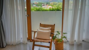 Ein Korbstuhl mit Kissen, ein Blumentopf und Blick auf eine Berglandschaft durch eine Glastür.