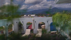 Eine Terrasse mit Liegestühlen und einem Tisch, mit Blick auf eine Berglandschaft und einen klaren Himmel.
