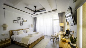 Ein modernes Hotelzimmer mit einem großen Bett, einem Schreibtisch mit Lampe, einem Fernseher und einem Deckenventilator.