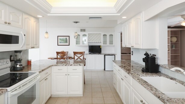 A modern kitchen with white cabinetry, a central island with chairs, a built-in oven, and a large sink.