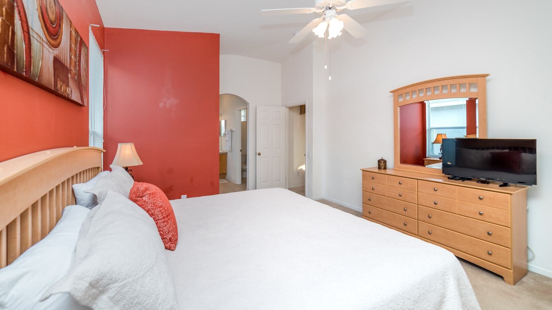 Un dormitorio con cama, cómoda, televisor y ventilador de techo.