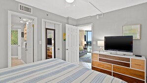 Un dormitorio con una cama, un televisor sobre un aparador y un ventilador de techo.