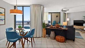 Una sala de estar moderna con comedor, ventanas amplias, ventilador de techo y vista al océano.