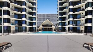 Un hotel moderno con piscina central, varios balcones y un edificio distintivo al fondo.