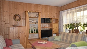 A wooden-paneled living room with a sofa, a television, and a wooden cabinet with glassware.